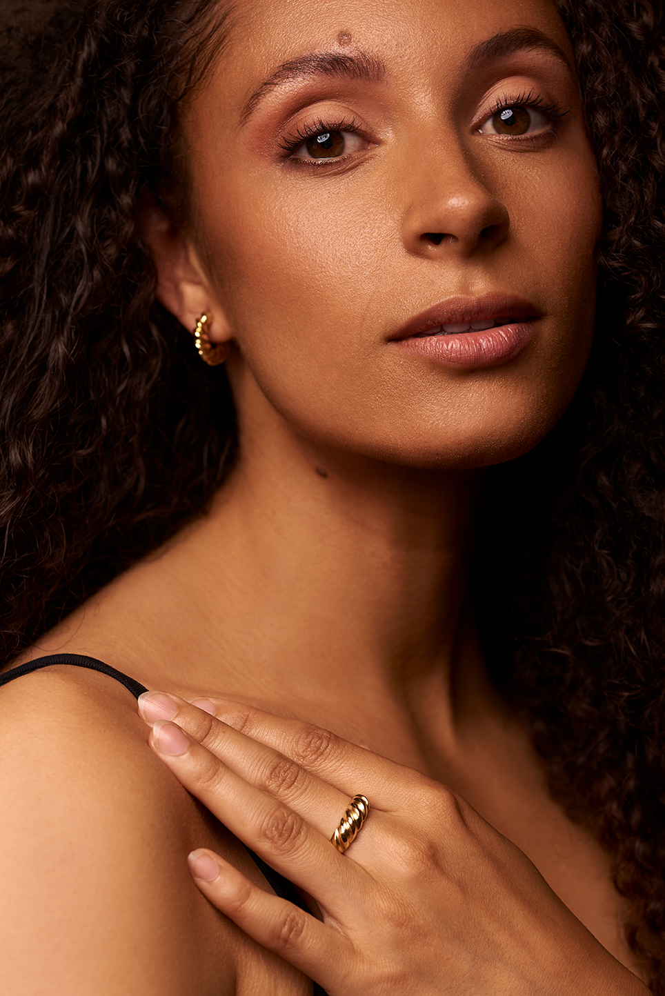 Model holding her hand on her shoulder to showcase her earring and ring.