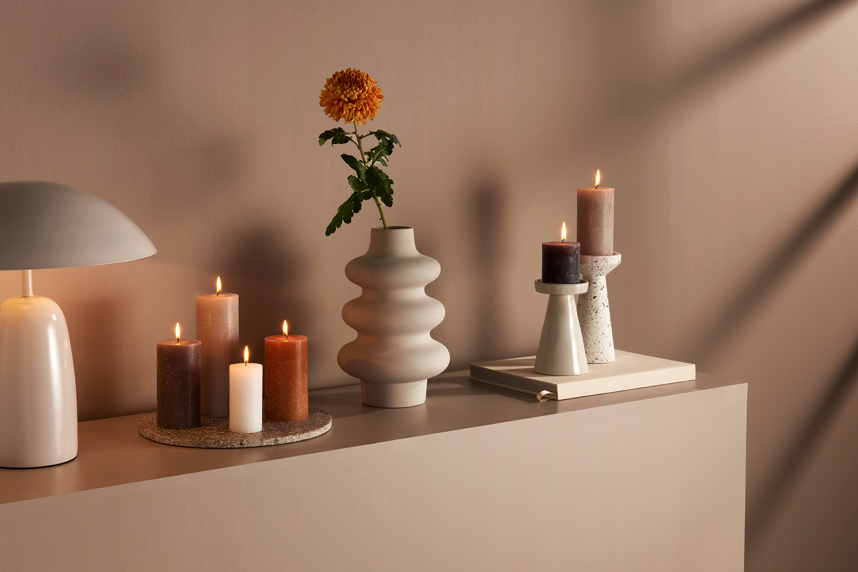 A cabinet with decoration pieces on it like a vase, lamp and candles from the brand Bolsius