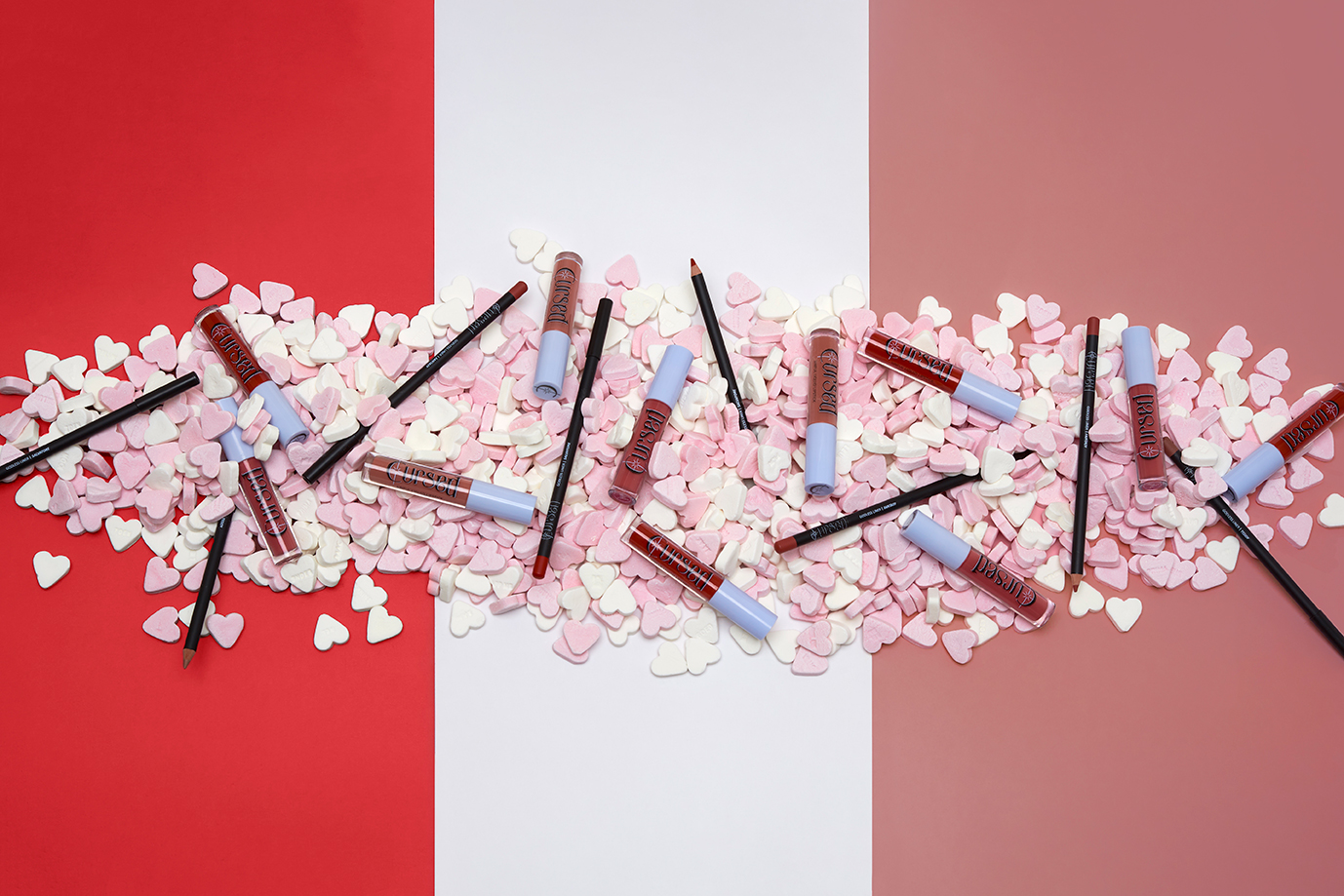 Make-up products on a red, white, pink background with sugar candy and the make-up products on the suger hearts.