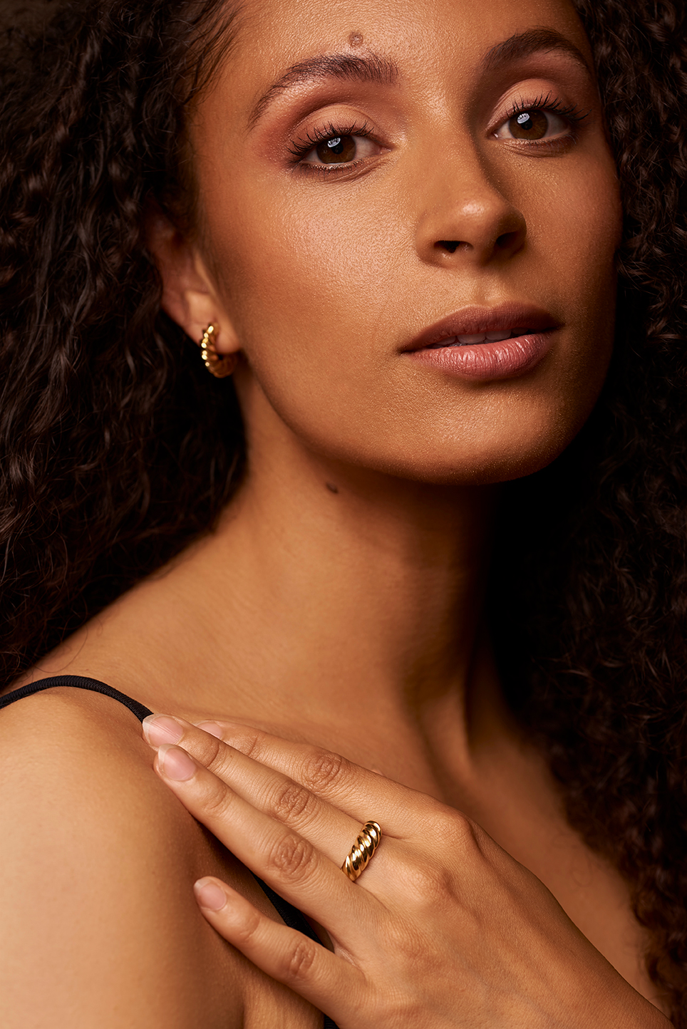 Model holding her hand on her shoulder to showcase her earring and ring.