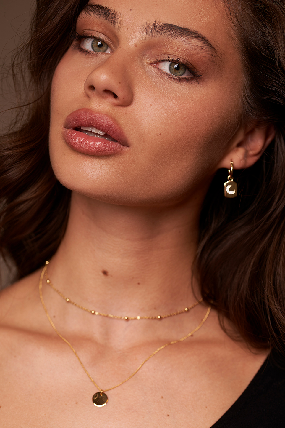 Model on a dark beige background showcasing different jewellery pieces.