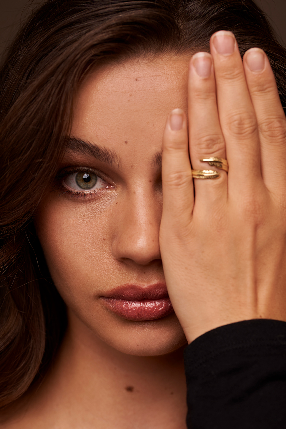 Model holding her hand in front of her eye to showcase a ring.