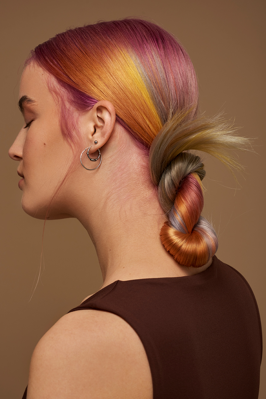 Photo in the studio on a beige background with colourful hair, having both Pink, Yellow and purple in her hair.