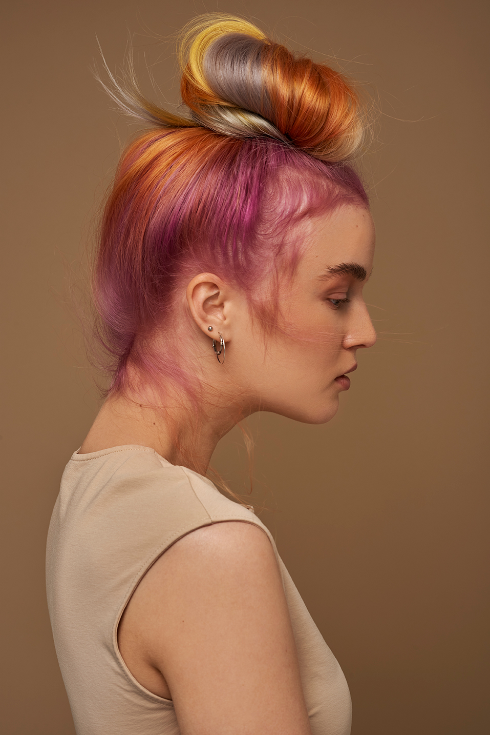 Photo in the studio on a beige background with colourful hair, having both Pink, Yellow and purple in her hair.