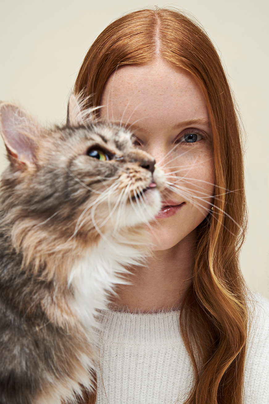 Model with a cat in front of her face. The cat is sticking her tong out.