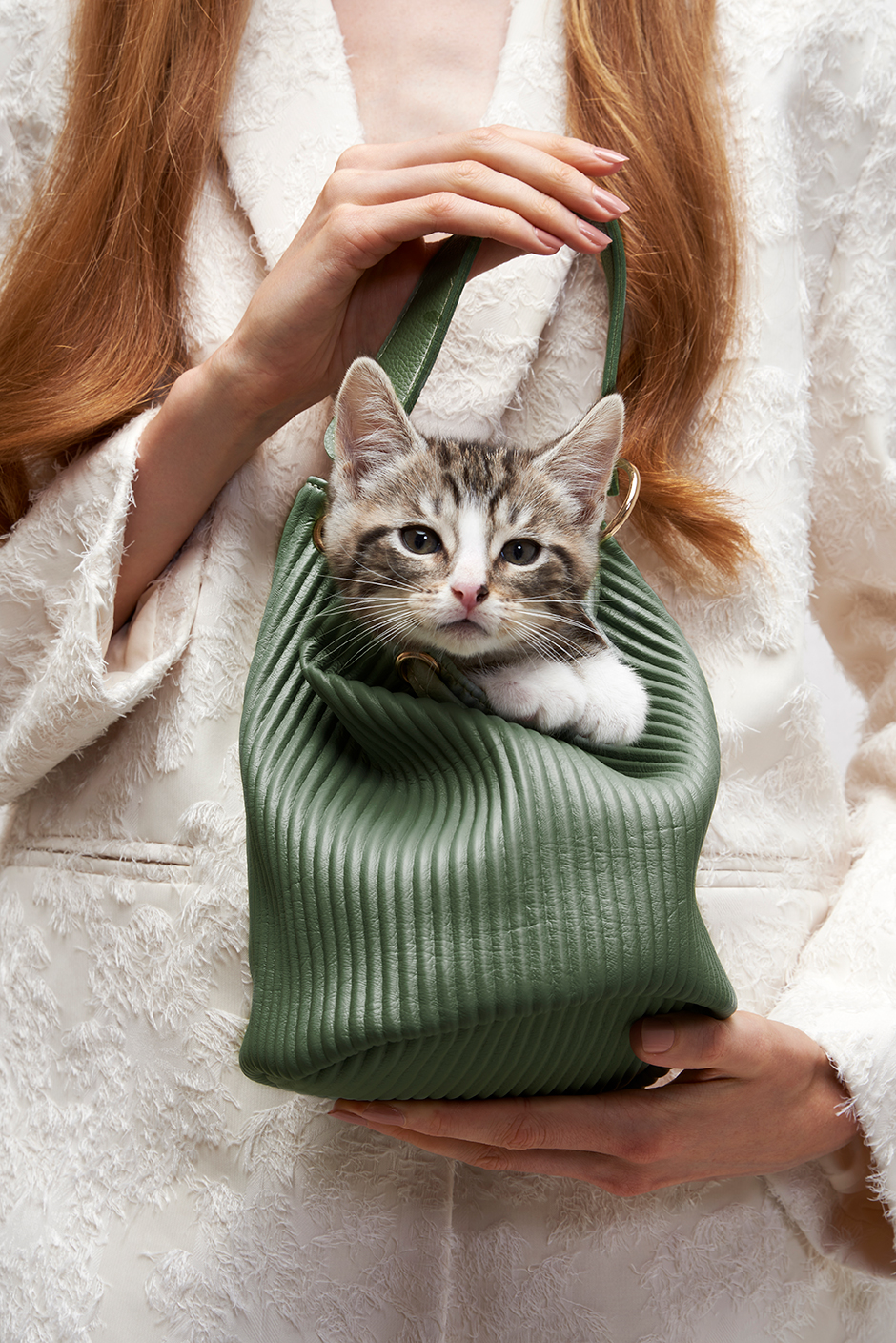 A model holding a bag with a kitten in it looking towards us.