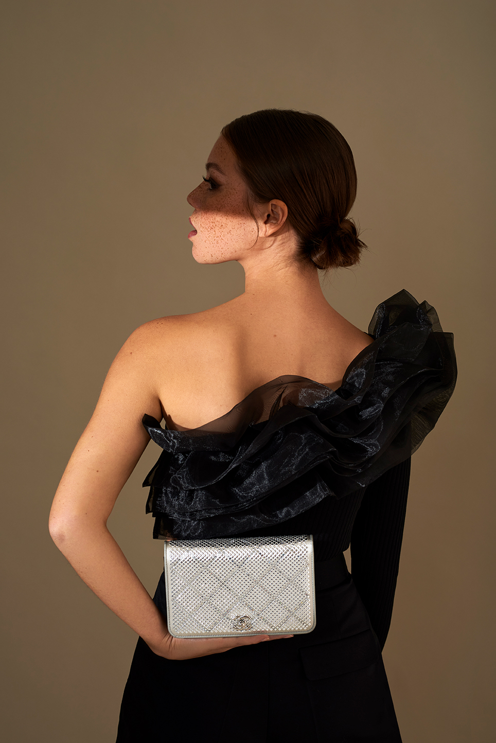 Model with focused light on her skin, lighting half of her face. She is holding a Chanelbag.