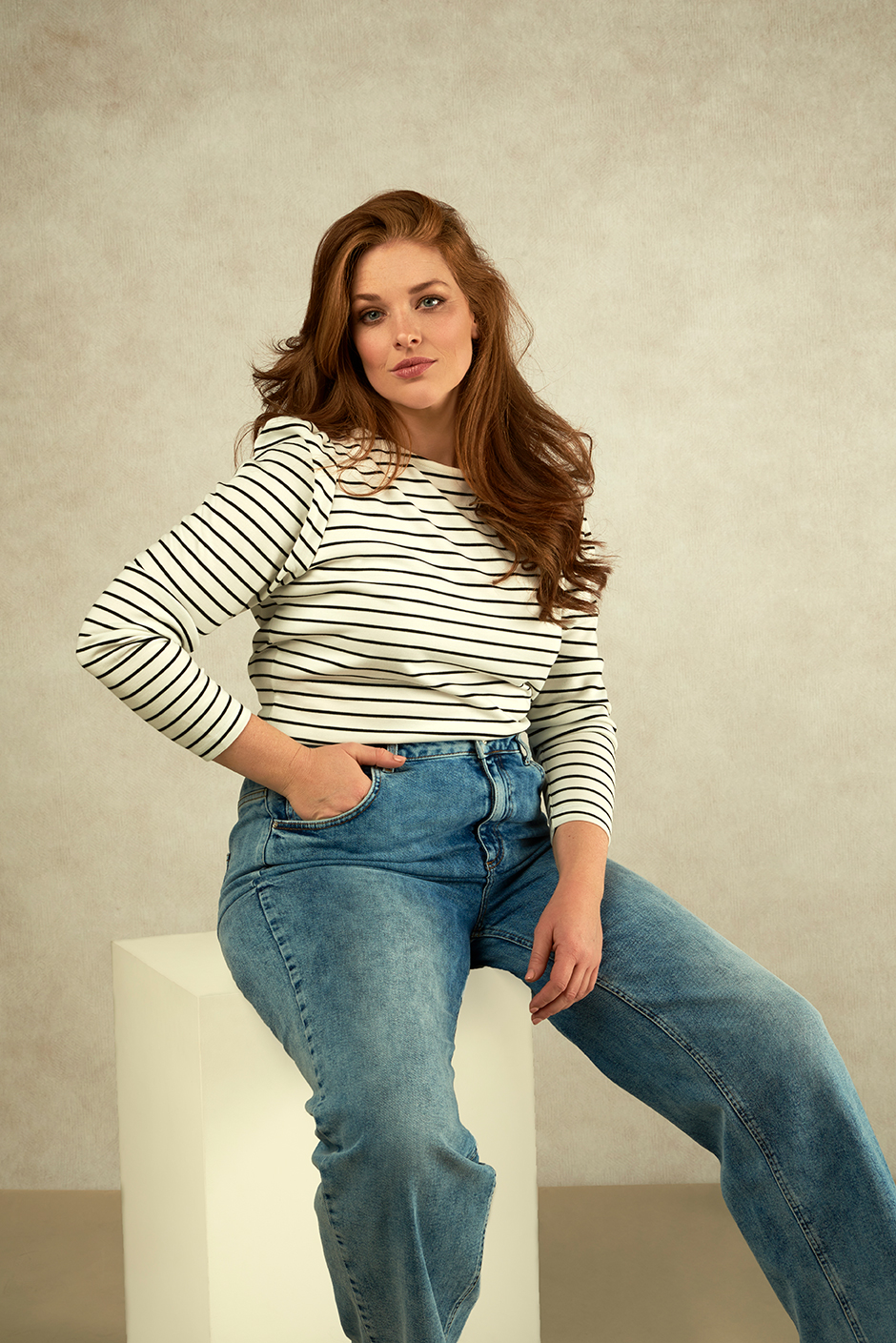 Plussize Model on a white wooden pilar on a textured background. Wearing stripes and jeans.